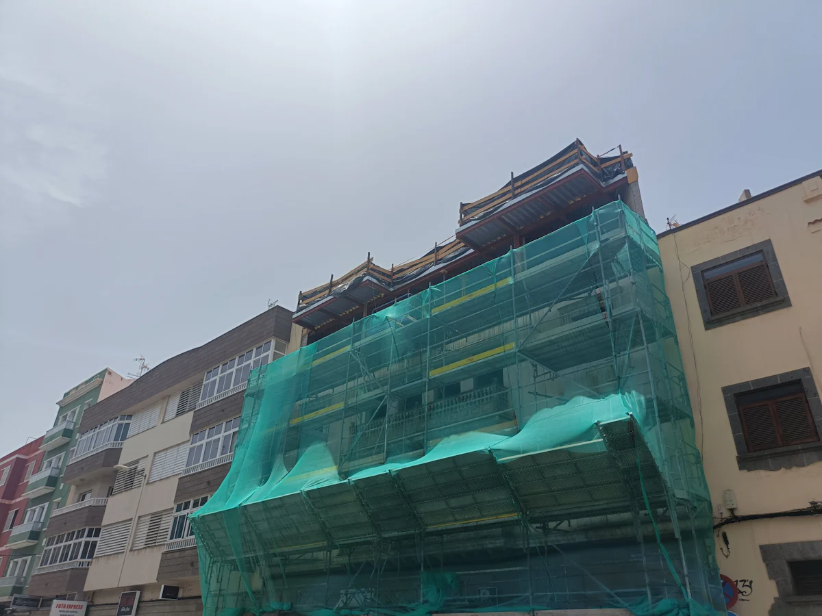 Immeuble sous échafaudage couvert d’un filet de protection pendant un ravalement de façade