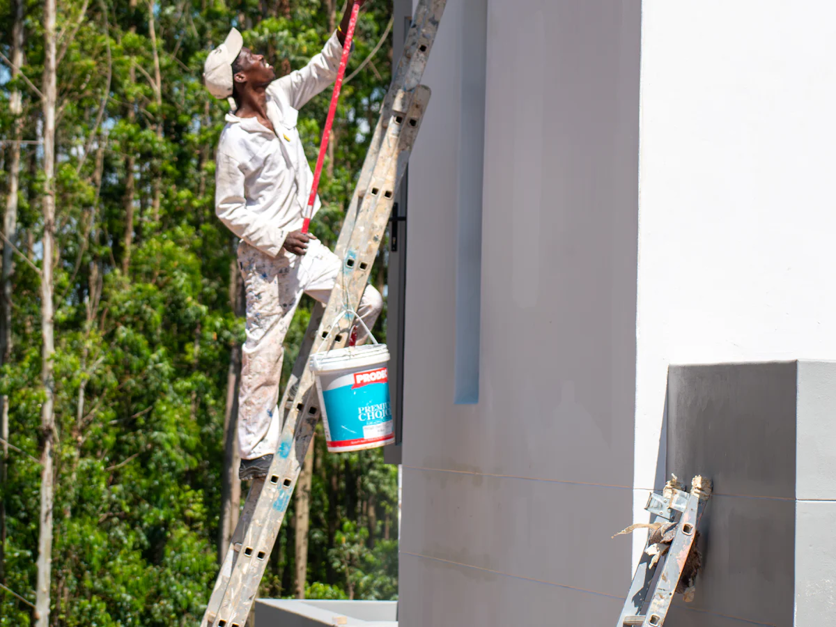 Peintre sur une échelle appliquant une peinture de façade au rouleau