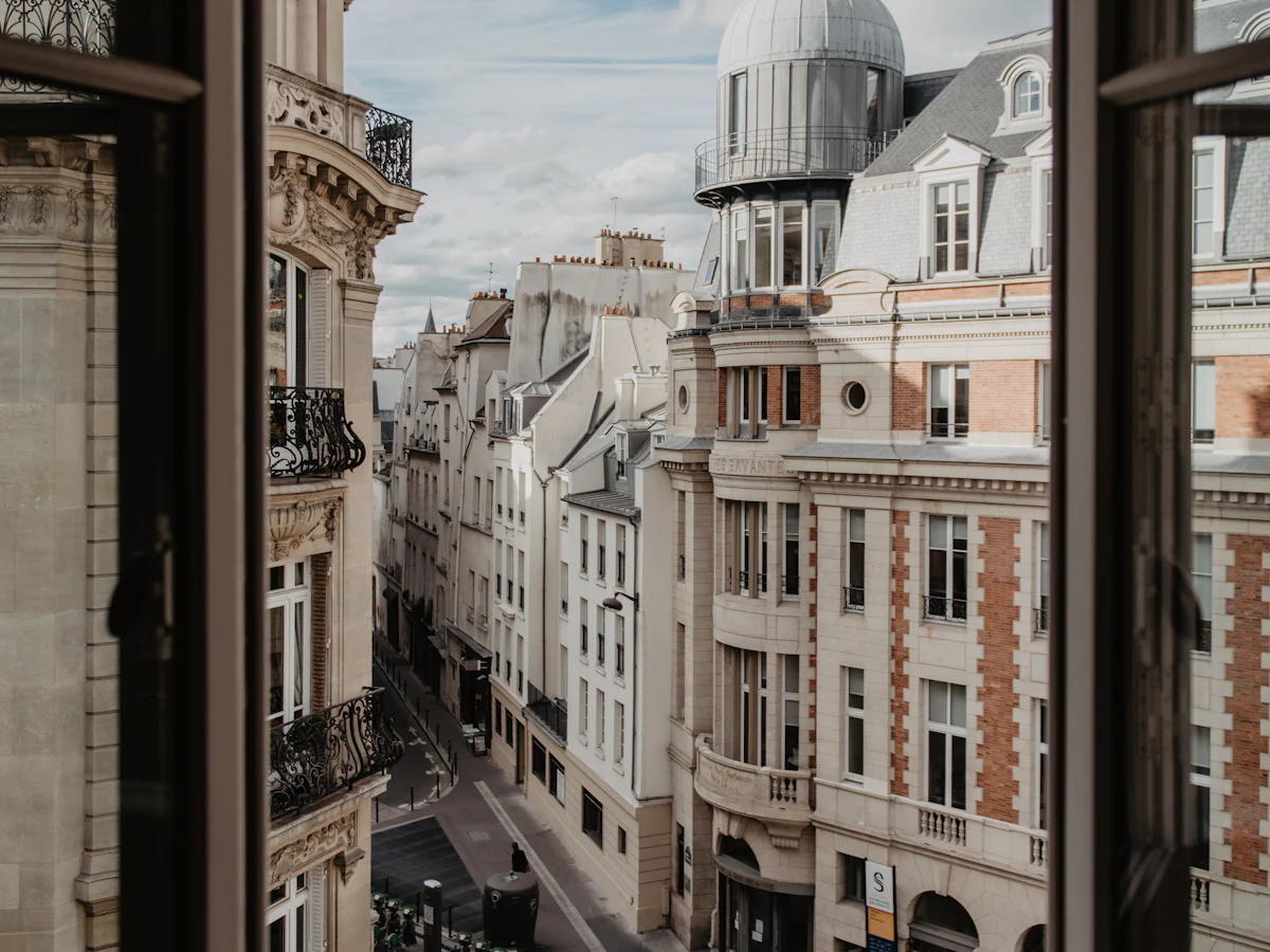 Rue parisienne vue depuis une fenêtre ouverte, façades en pierre et en brique